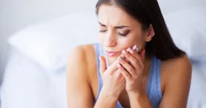 A young woman wincing in pain while holding her jaw and cheek, indicating a dental emergency requiring immediate dental care